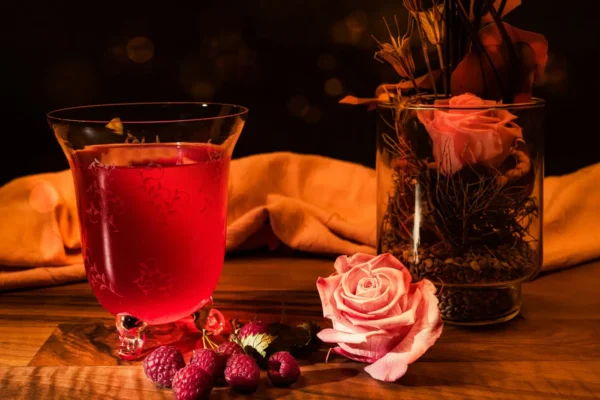 red liquid in clear drinking glass beside pink rose bouquet